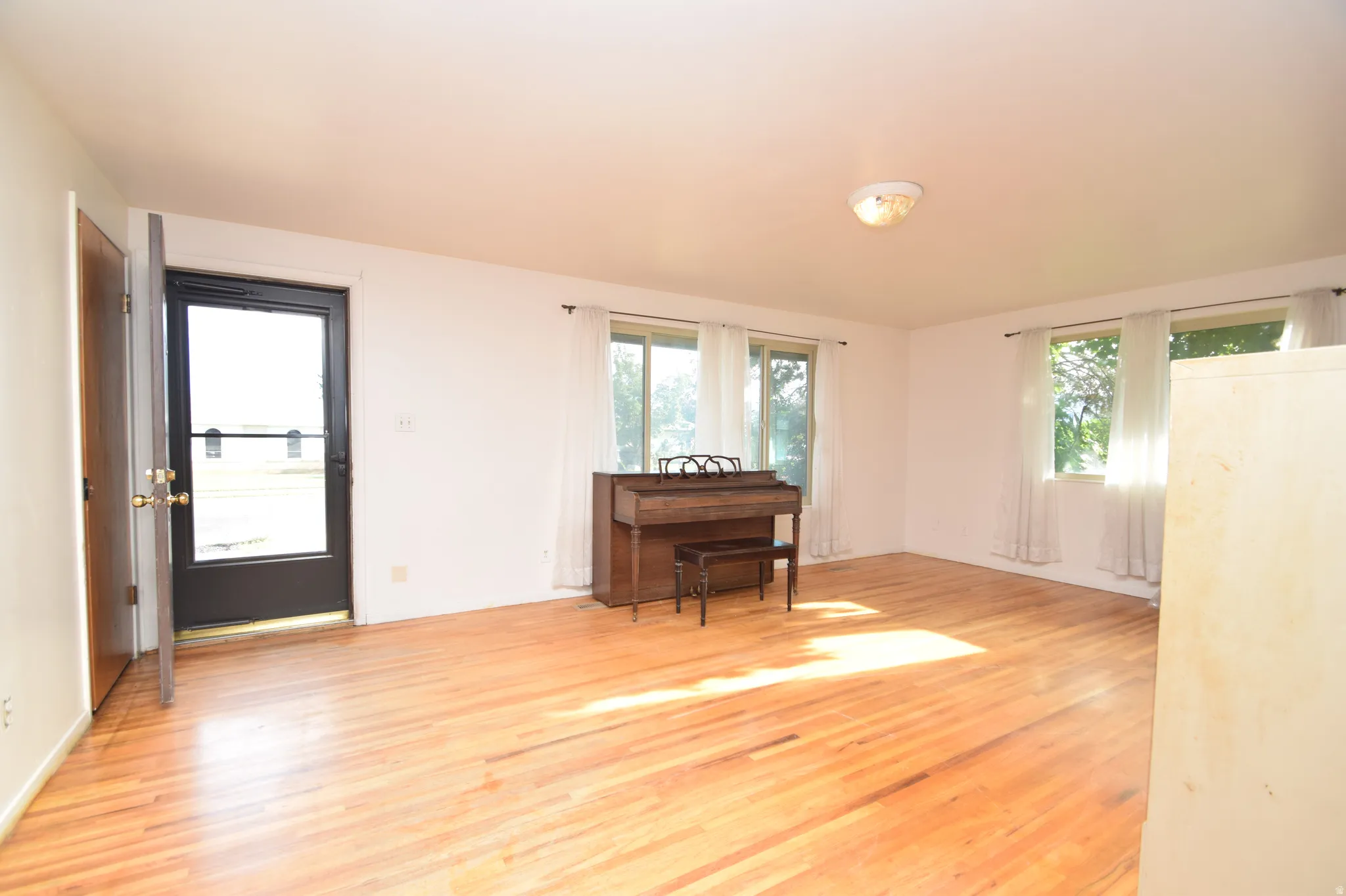 Hardwood flooring throughout, multiple windows with curtains, and a flush-mount ceiling light fixture