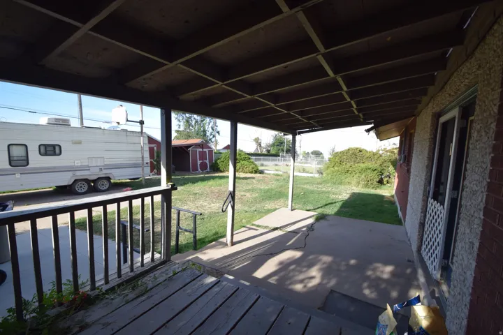 Covered patio with a concrete slab, wood deck, and a wooden railing