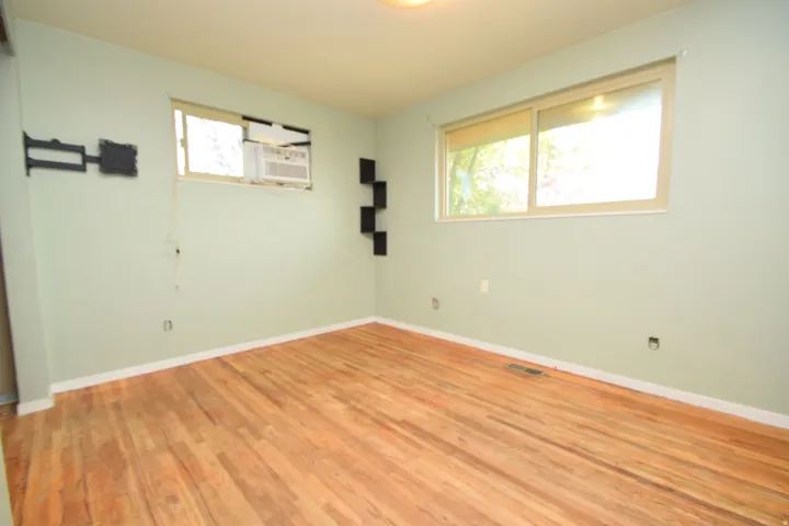 Hardwood flooring, multiple windows providing natural light, and a built-in wall-mounted air conditioning unit