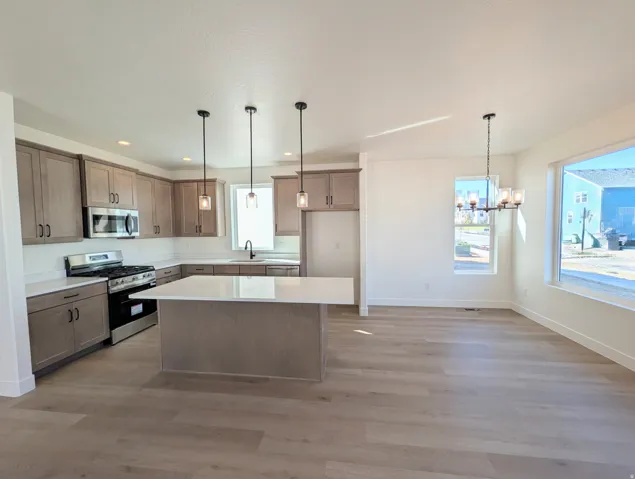 Modern kitchen featuring wood-finish flooring, light cabinetry, white countertops, stainless steel appliances, and pendant lighting