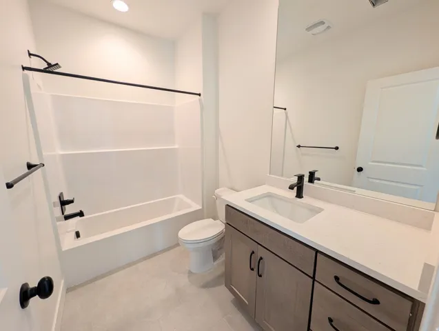 Modern bathroom featuring a single vanity with a white countertop and rectangular sink, a built-in tub with a shower, and gray tile flooring