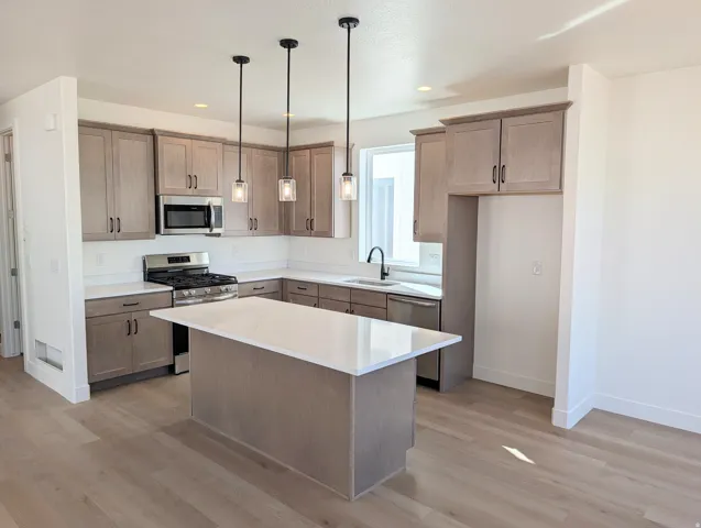 Kitchen featuring wood-finish flooring, an island with a light-toned countertop, stainless steel appliances, and pendant lighting