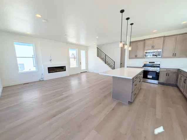 Open-concept living space featuring wood-finish flooring, a linear fireplace, and a kitchen island with pendant lighting