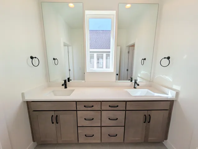 Dual vanity with integrated sinks, light-toned countertop, and wood-finish cabinetry featuring matte black hardware