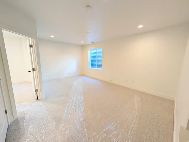 Recessed lighting illuminates a spacious room featuring light-toned carpeting and a window with blinds