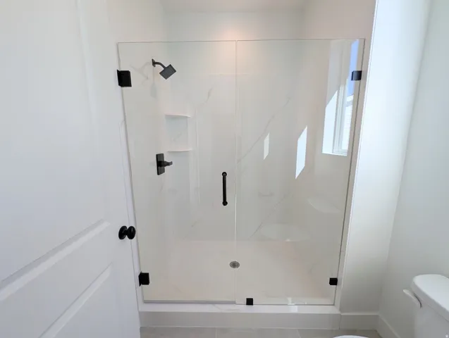 Frameless glass shower with matte black fixtures, white tile surround, integrated shelving, and a built-in bench