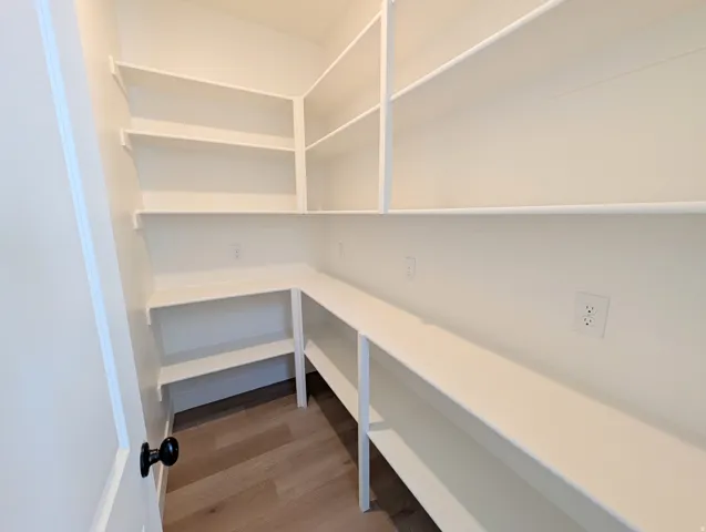 Walk-in pantry featuring extensive white shelving, wood-finish flooring, and multiple electrical outlets