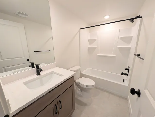 Bathroom featuring a wood-finish vanity with a rectangular sink, a white countertop, and a built-in tub with a shower