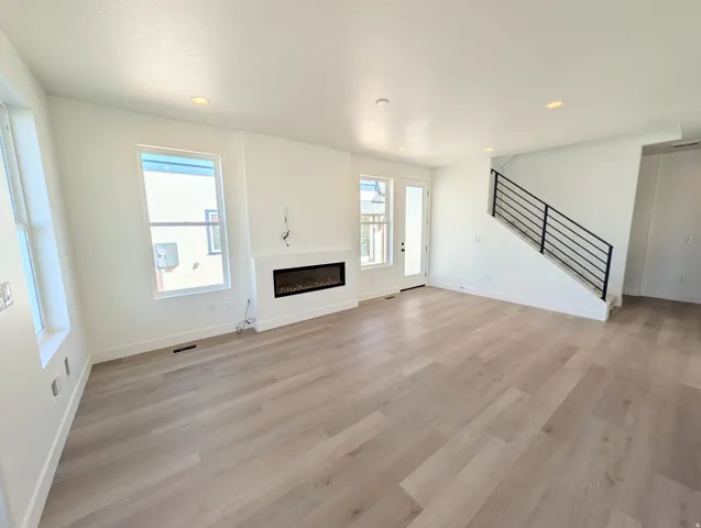 Spacious living area featuring light wood-finish flooring, a contemporary electric fireplace, multiple windows, recessed lighting, and a modern staircase with black iron railings