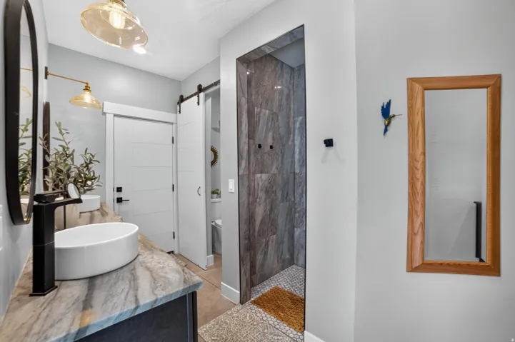 Vanity with vessel sink, stone countertop, matte black faucet, and pendant lighting