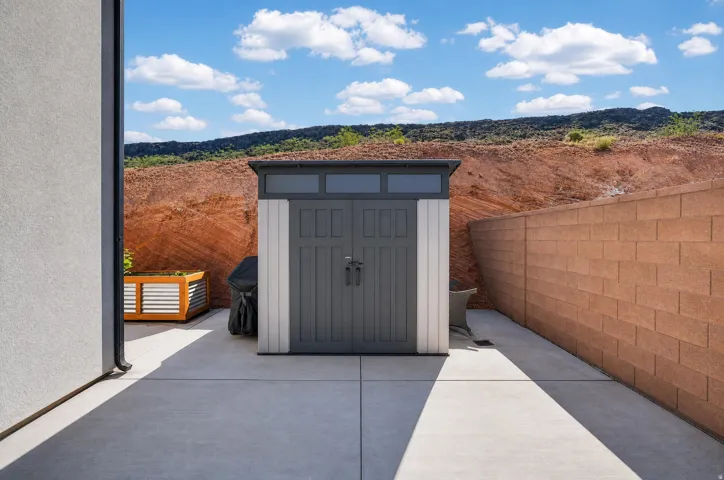 Paved concrete patio area featuring a storage shed, a block wall, and a raised planter box