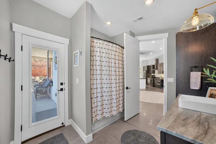 Full-lite exterior door, built-in shower, recessed lighting, concrete flooring, and a rectangular vessel sink