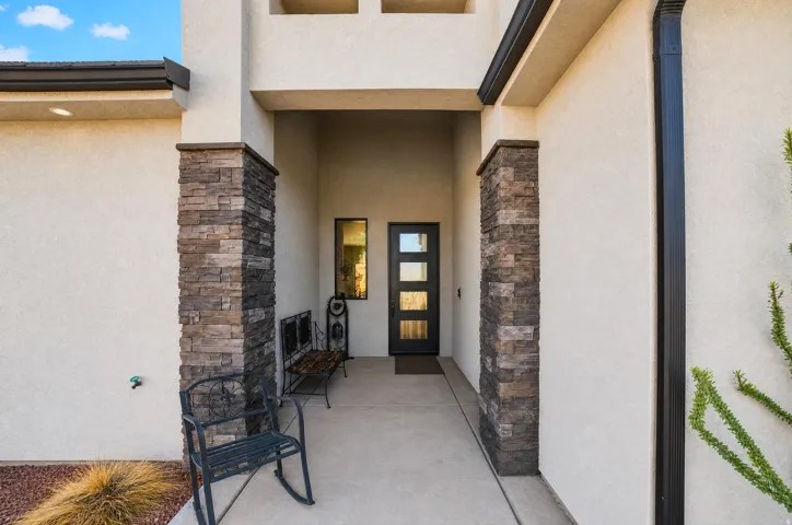 Recessed entry with stone veneer columns, stucco exterior, and a modern dark-framed entry door with frosted glass inserts