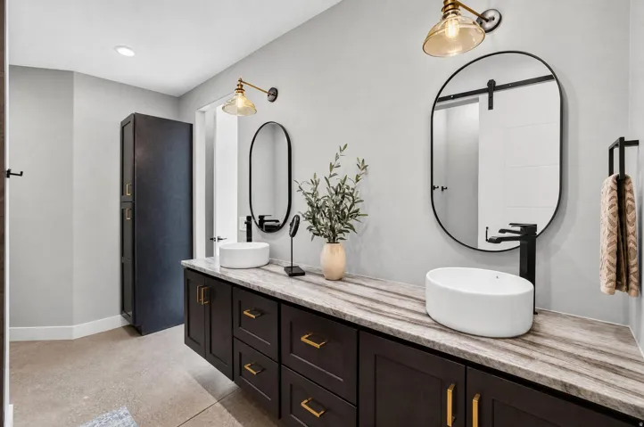 Floating vanity with double vessel sinks, stone countertop, matte black fixtures, and oval mirrors