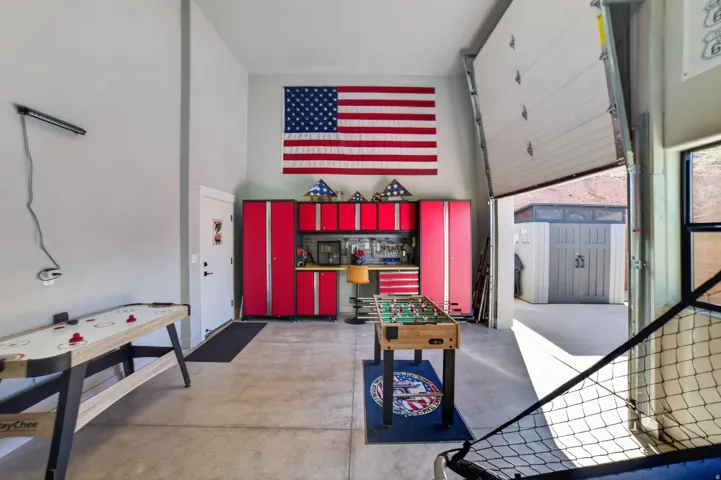 Concrete flooring, high ceilings, red storage cabinetry, built-in workbench, and a roll-up garage door