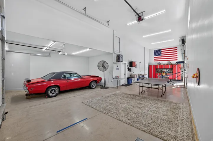 Spacious garage with high ceilings, concrete flooring, built-in cabinetry, and overhead lighting