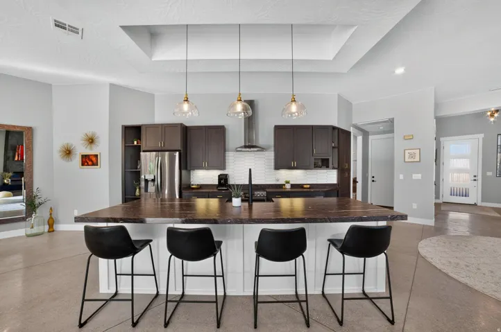 Central kitchen island with seating, stainless steel appliances, dark wood-finish cabinetry, subway tile backsplash, and a coffered ceiling with pendant lighting