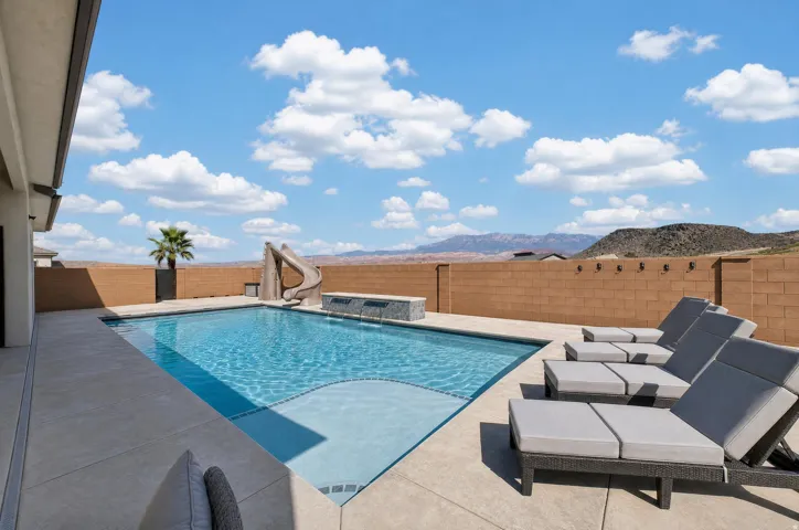 Rectangular swimming pool with integrated slide, light-colored pool deck, and a privacy wall