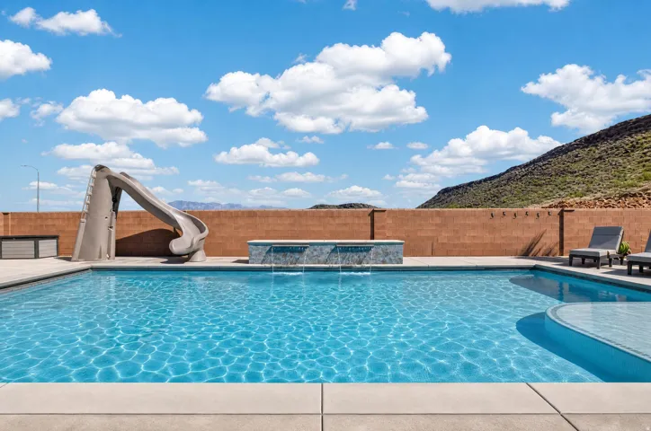 Rectangular swimming pool featuring a curved sun shelf, integrated spa with waterfall features, and a concrete patio surround