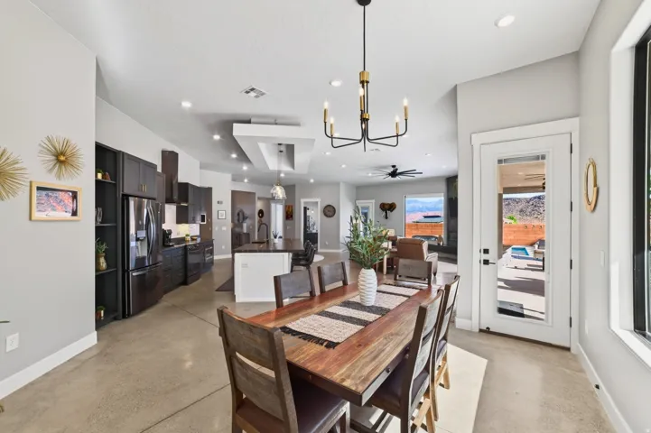Spacious open-concept living area featuring a modern kitchen with dark cabinetry and stainless steel appliances, a dining area with a contemporary chandelier, and concrete flooring throughout