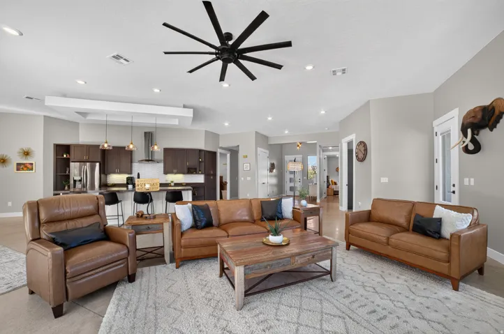 Open-concept living area featuring a kitchen with dark wood-finish cabinetry, a large kitchen island with counter seating, pendant lighting, and a contemporary ceiling fan