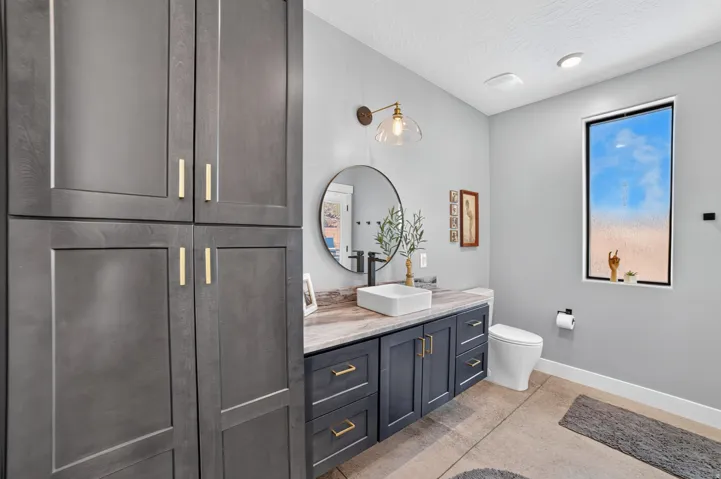 Built-in cabinetry with gold-finish hardware, vessel sink, wall-mounted light fixture, and large rectangular window