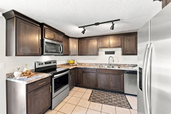 Kitchen featuring dark wood-finish cabinetry, stainless steel appliances, speckled countertops, and tile flooring