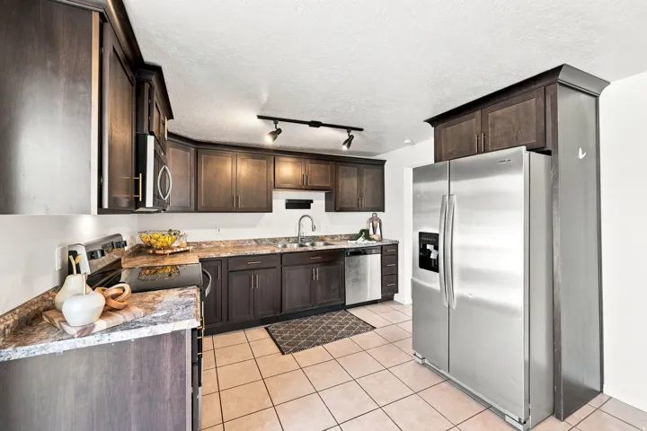 Kitchen featuring dark wood-finish cabinetry, stainless steel appliances, speckled countertops, and track lighting