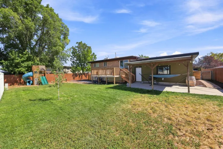Spacious backyard featuring a covered patio, concrete hardscaping, wood deck, and wood fencing