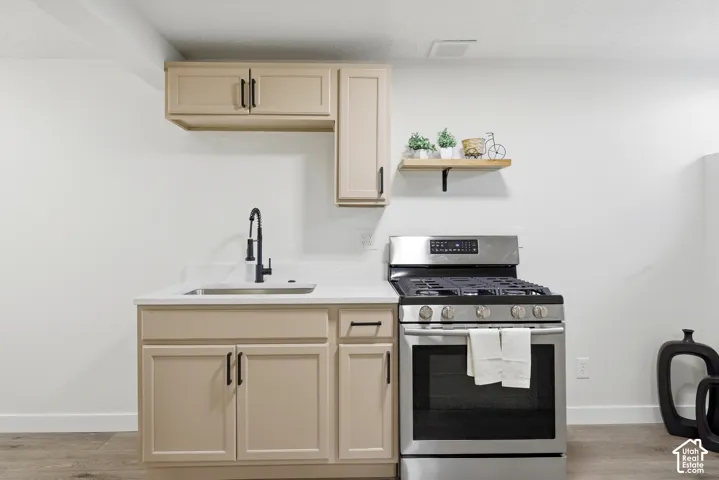 Stainless steel gas range, light-toned cabinetry with matte black hardware, single basin sink with a matte black faucet, and white countertops