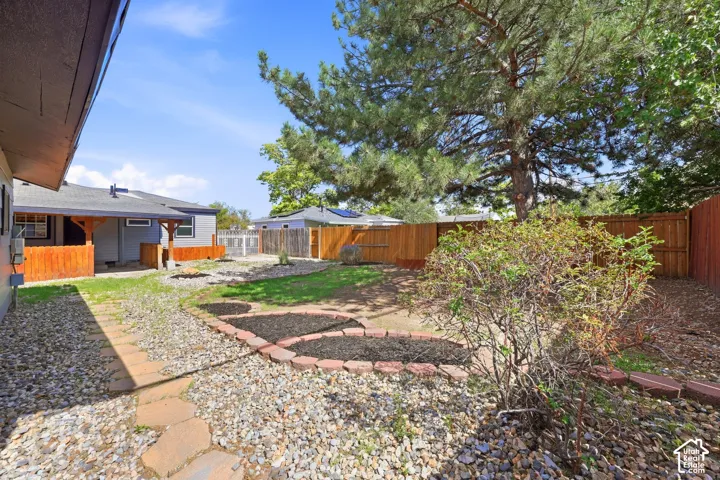 Expansive backyard featuring a covered patio, wood fencing, mature trees, and landscaping elements with stone and brick borders