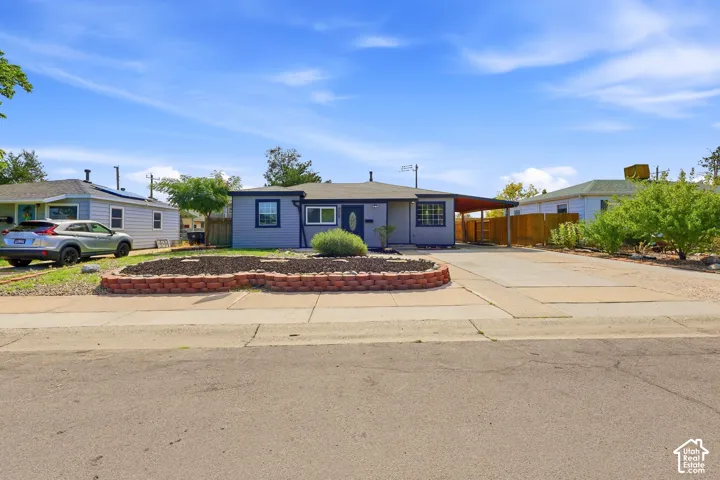 Single-story residence featuring a covered carport, concrete driveway, and a front yard with a brick-edged planting bed