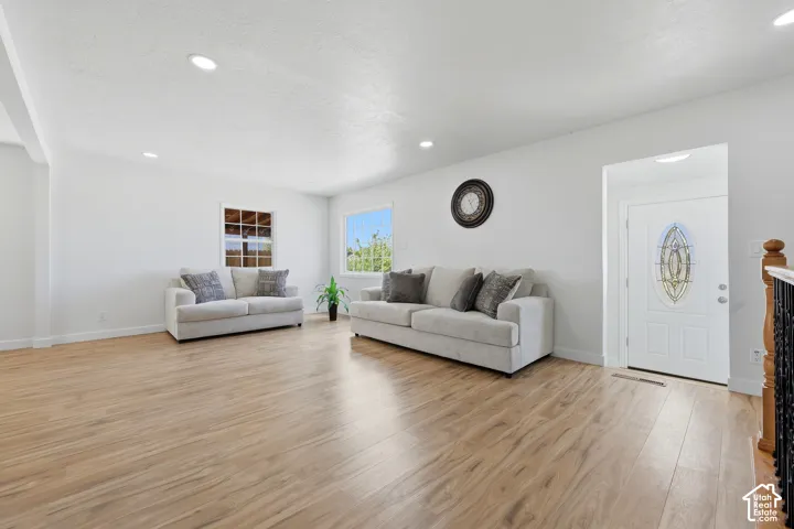 Recessed ceiling lighting, wood-finish flooring, white walls, multiple windows, and a decorative front entry door