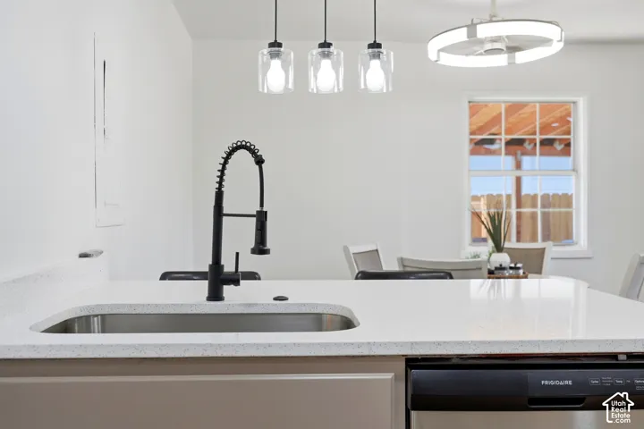 Kitchen island featuring a stainless steel sink, matte black pull-down faucet, light-toned countertop, and integrated dishwasher
