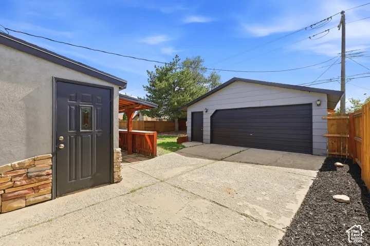 Detached two-car garage with a side entry door, concrete driveway, and a separate outbuilding with stone veneer accents