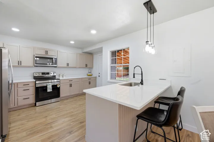 Kitchen featuring wood-finish flooring, white countertops, stainless steel appliances, and an island with a sink and pendant lighting