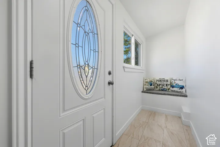 Entryway featuring a white paneled door with an oval decorative glass insert, a window with white trim, and light-toned tile flooring
