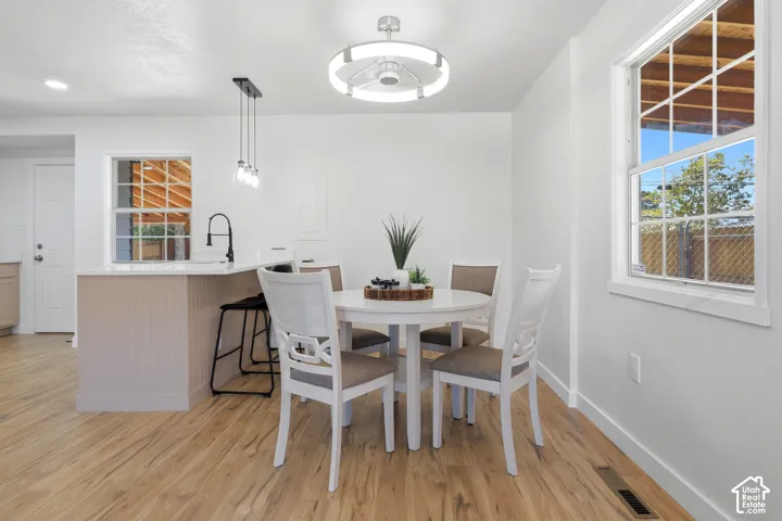 Wood-finish flooring, white walls, modern ceiling light fixture, kitchen island with beadboard paneling, and a contemporary pendant light