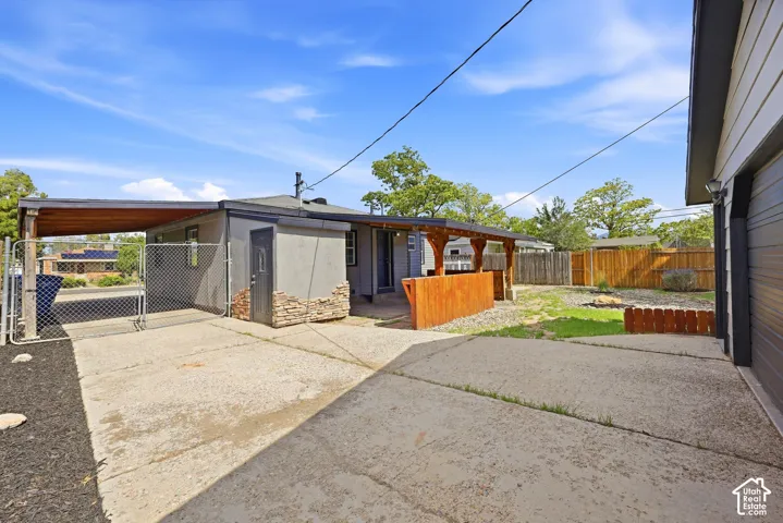 Concrete driveway and patio space, covered carport, fenced yard, and a separate structure with stone veneer detailing
