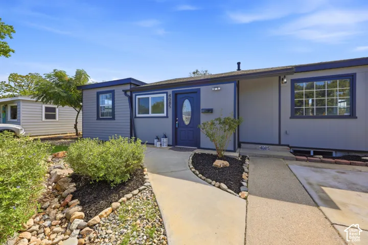 Gray exterior siding with contrasting dark trim, a deep blue entry door with an oval window, and a concrete pathway leading to the entrance