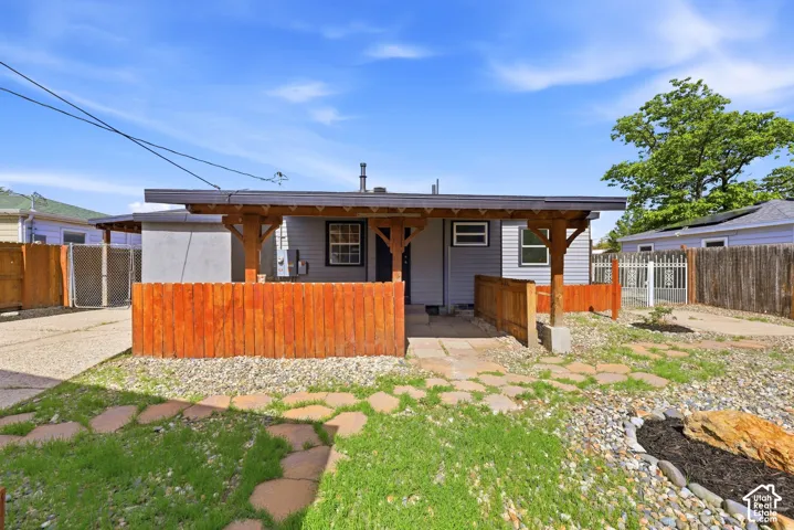 Covered entry porch with wood columns, gravel and stone paver landscaping, wood privacy fence, and paved driveway