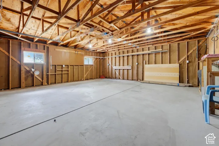 Spacious garage with exposed wood rafters, concrete flooring, and multiple windows providing natural light