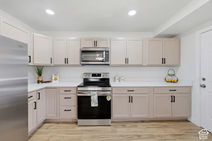 Kitchen featuring wood-finish flooring, white countertops, light-colored cabinetry with black hardware, and stainless steel appliances