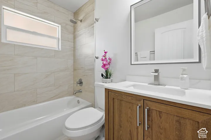 Bathroom featuring a white bathtub, tiled shower surround, wood-finish vanity with a white countertop, and a contemporary mirror with integrated lighting