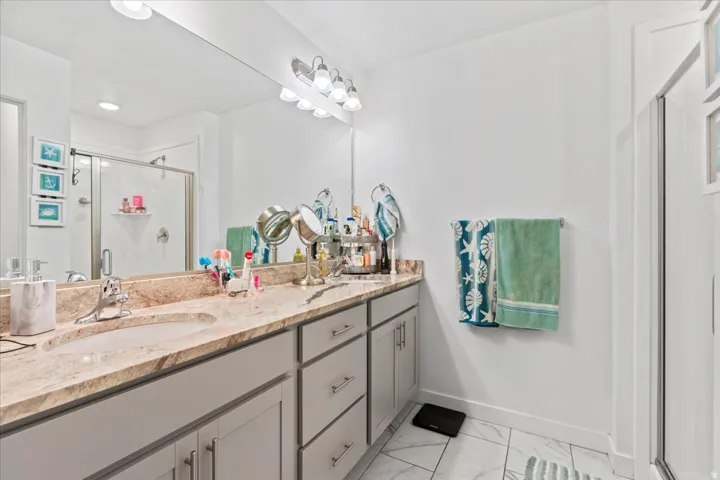 Dual sink vanity with light-toned countertop, large wall-mounted mirror, and overhead vanity lighting