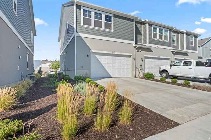 Exterior featuring a multi-story design with siding and stucco finishes, attached garage, concrete driveway, and front landscaping with ornamental grasses and shrubs