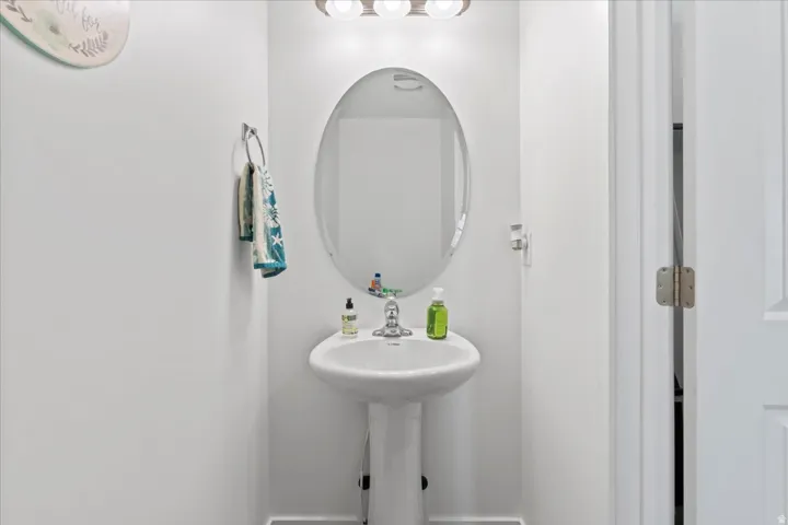 Pedestal sink with a polished chrome faucet, oval mirror, and wall-mounted vanity light