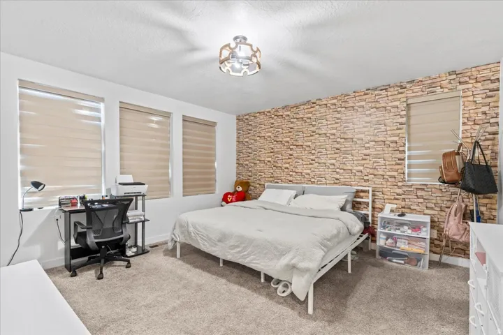 Textured accent wall, multiple windows, plush carpet flooring, and a contemporary ceiling fixture