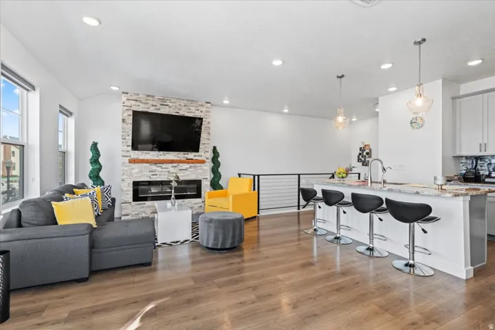 Open-concept living area featuring wood-finish flooring, a stacked stone fireplace, recessed lighting, and a kitchen island with pendant lighting