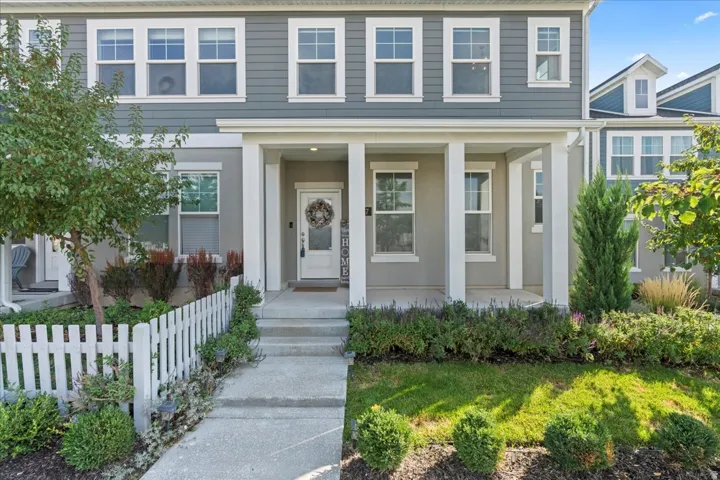 Gray horizontal siding with white trim, covered front porch, white picket fence, concrete walkway, and landscaped front yard